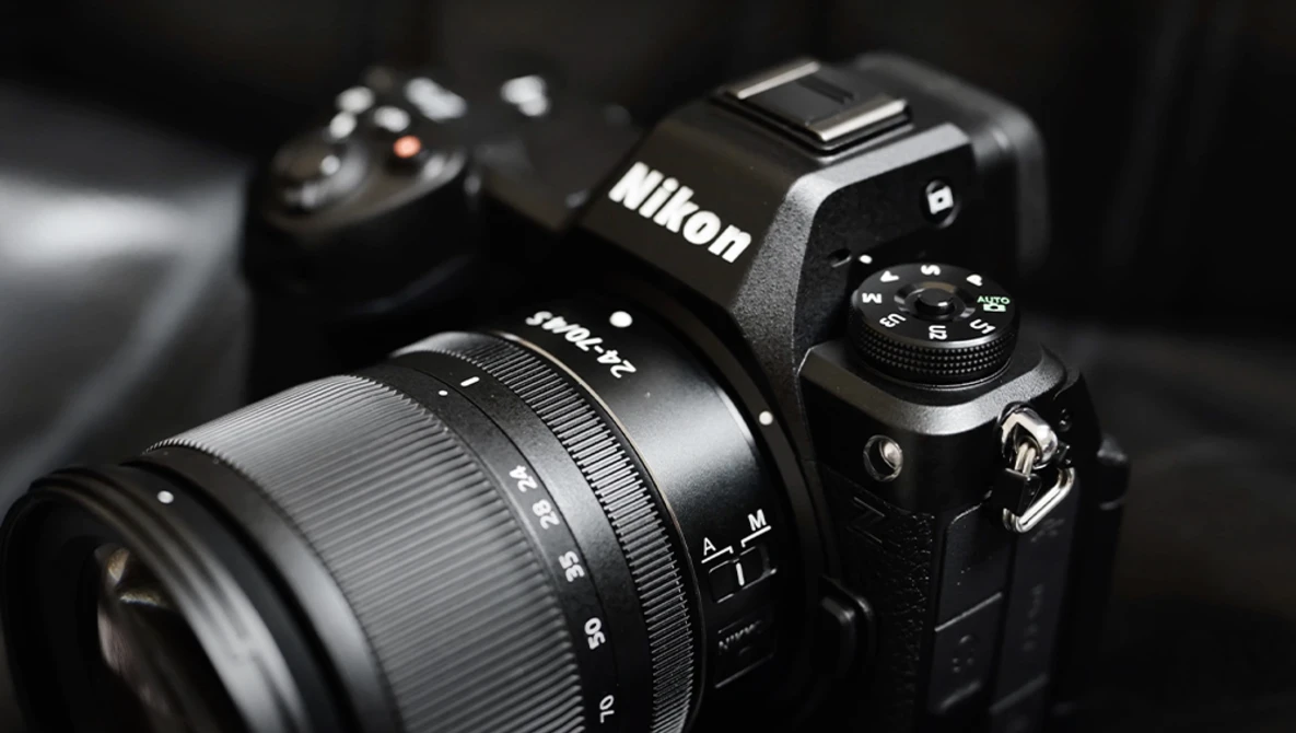 Nikon DSLR camera with attached zoom lens on dark background with secondary camera blurred in background.