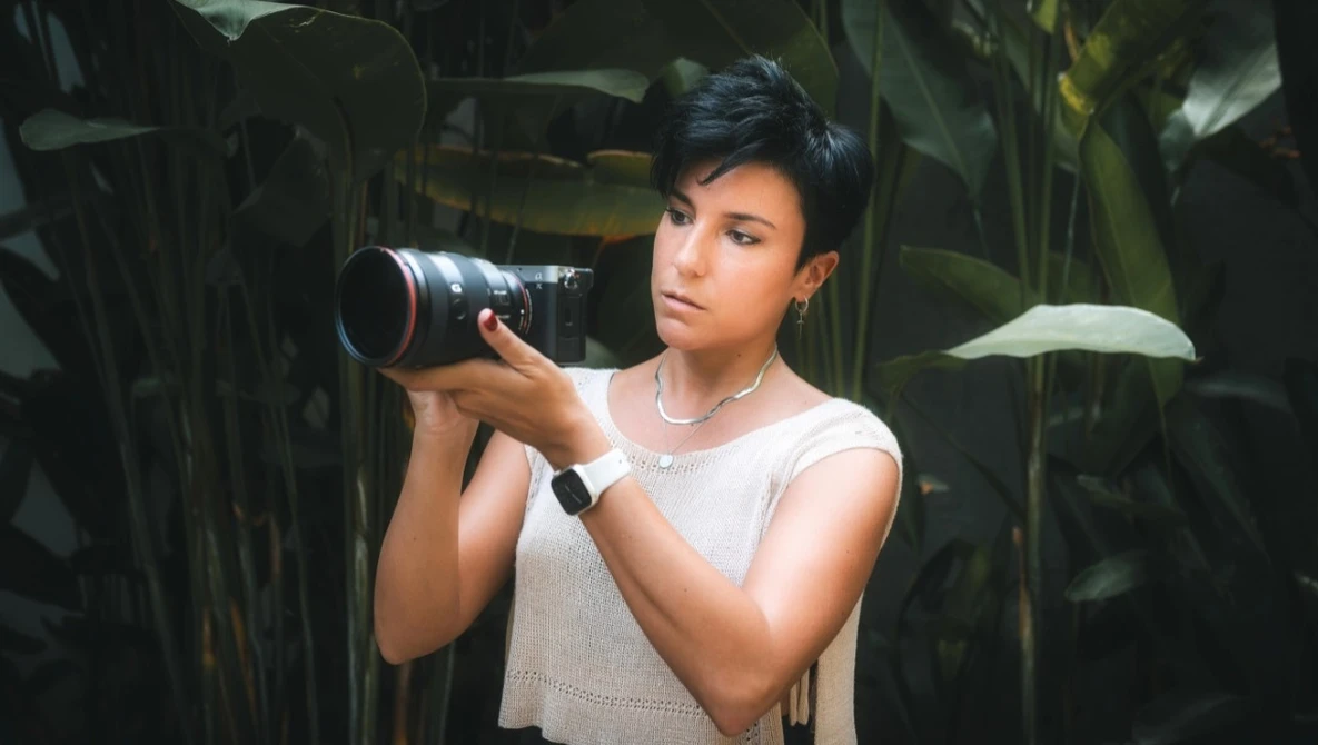 Photographer with telephoto lens among lush green foliage, composing a shot.