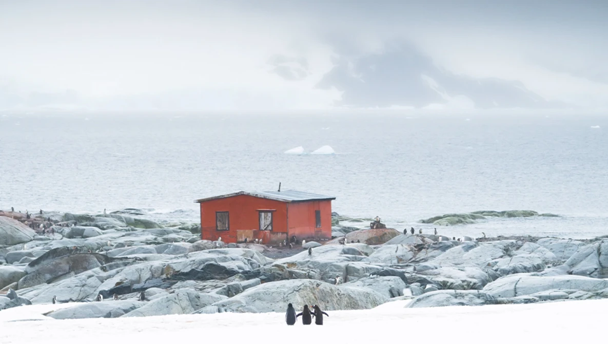 Bright red building on snow-covered rocky terrain with ocean and sky beyond.