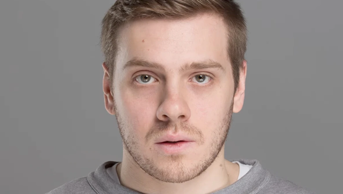 Portrait of a man with short brown hair against a neutral gray background.