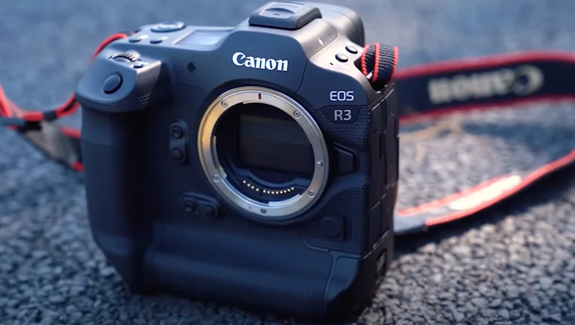 Canon EOS R3 mirrorless camera body without lens, displayed from front with open mount and red camera strap visible.