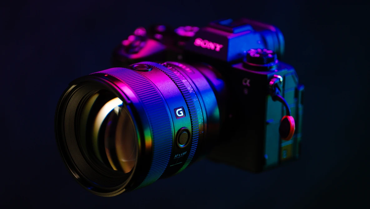 Sony mirrorless camera and lens illuminated with neon magenta and blue lighting against a dark background.