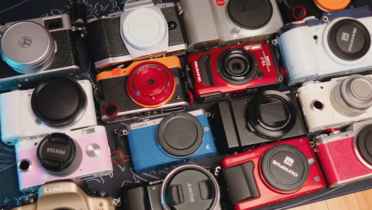 Overhead flat lay of approximately 20 compact and digital cameras in various colors arranged closely together.