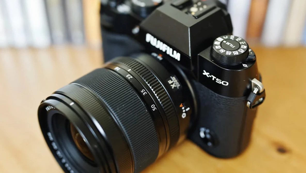 Fujifilm X-T50 mirrorless camera with attached zoom lens on wooden surface.