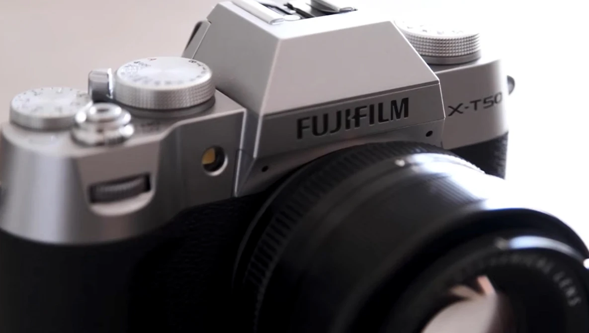Fujifilm X-T50 mirrorless camera with silver top plate and black lens attached, shot against neutral background.