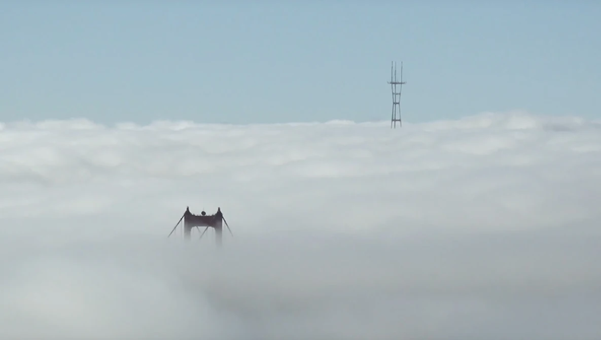 Golden Gate Bridge towers emerging from dense fog with a communications tower visible in the background.