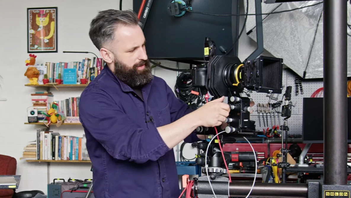 Cinematographer operating a large format film camera mounted on a rig in a studio setting.