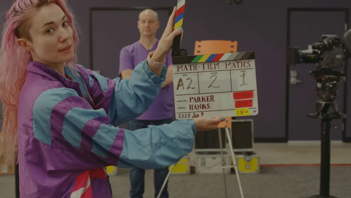 Woman with pink hair holding a colorful rainbow pride flag during a film production shoot.