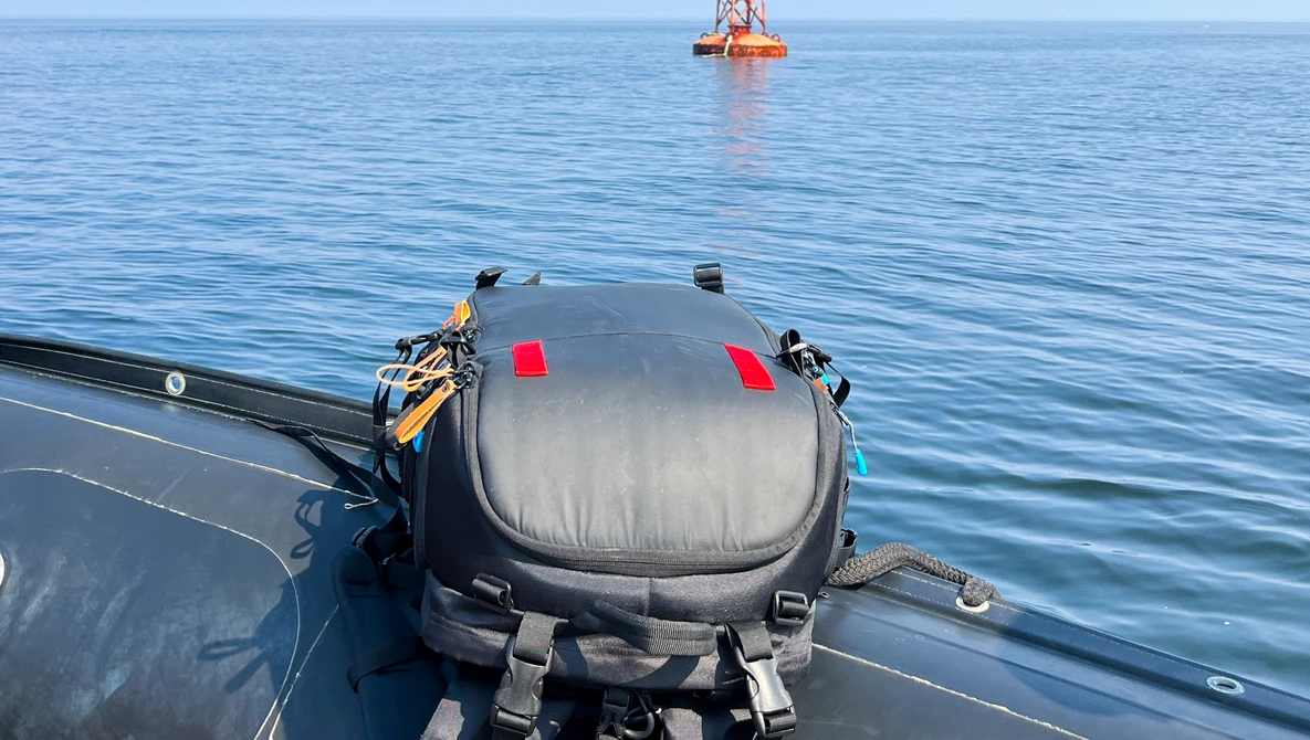 Submersible vessel mounted on a ship deck with offshore platform visible in calm blue water.