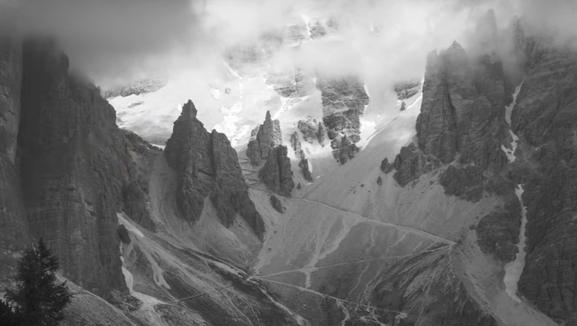 Dramatic black and white mountain landscape with towering rock formations and snow-capped peaks shrouded in clouds.