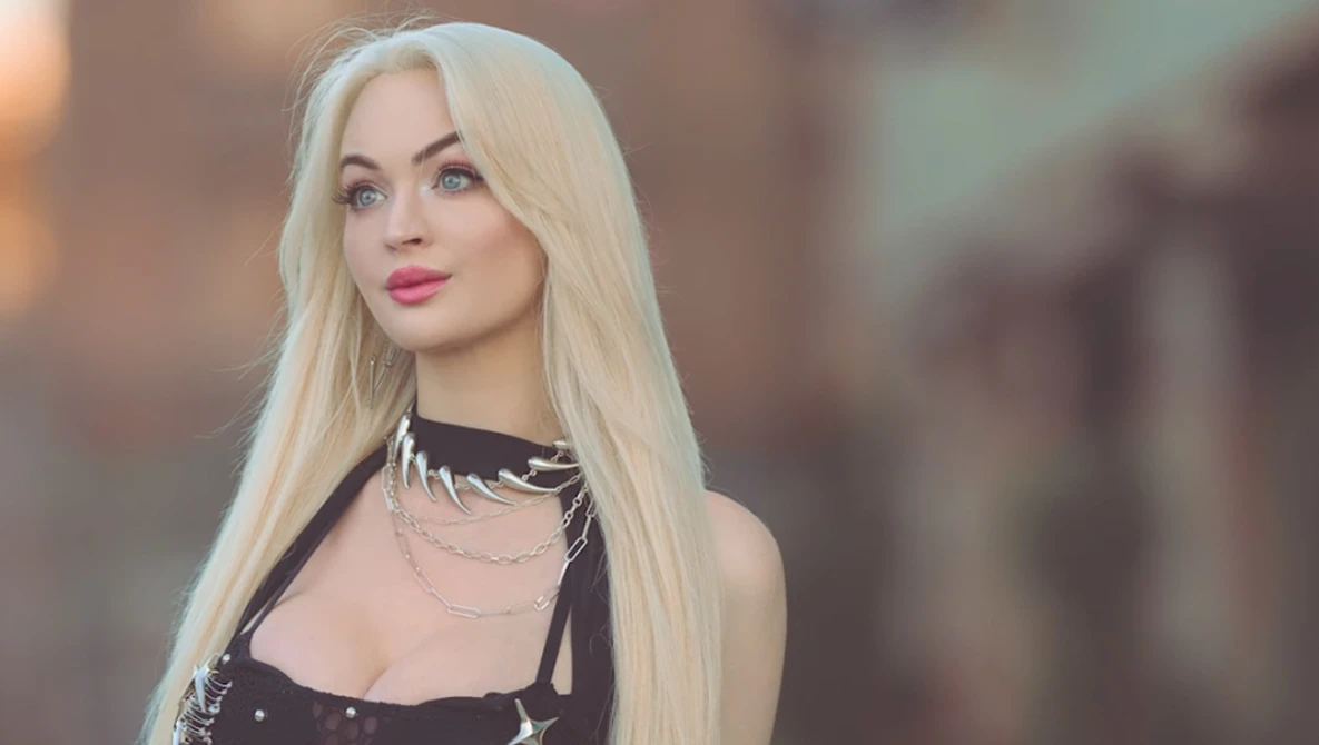 Blonde woman with long straight hair wearing black choker and star-patterned top against blurred urban background.