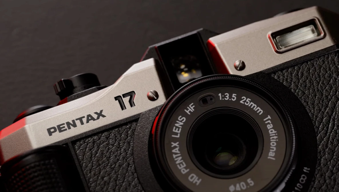 Pentax 17 film camera with red and white body and black leather grip, showing 25mm lens and built-in flash.