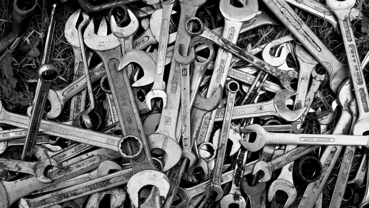 Overhead black and white arrangement of various wrenches and hand tools scattered densely across the frame.