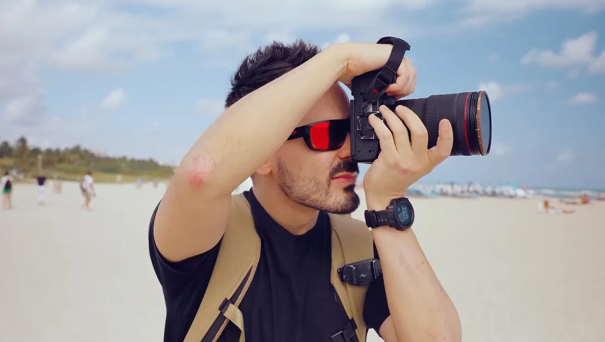 Photographer holding a DSLR camera with telephoto lens at the beach during daytime.