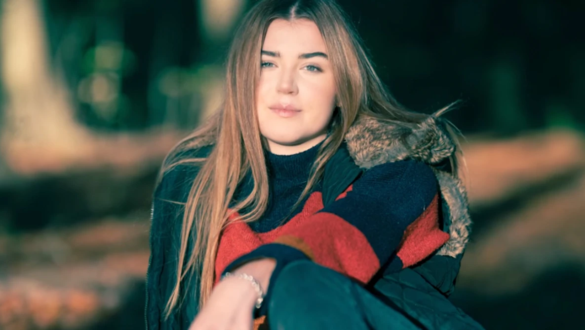 Woman with long brown hair holding a tabby cat while wearing a dark sweater with red accents.