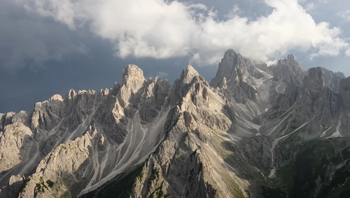 Dramatic limestone peaks of the Dolomites with layered ridges under cloudy sky.