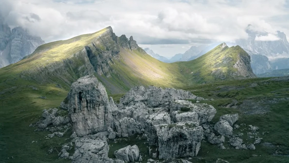 Alpine valley landscape with distinctive layered mountain peaks and weathered limestone rock formations in foreground.