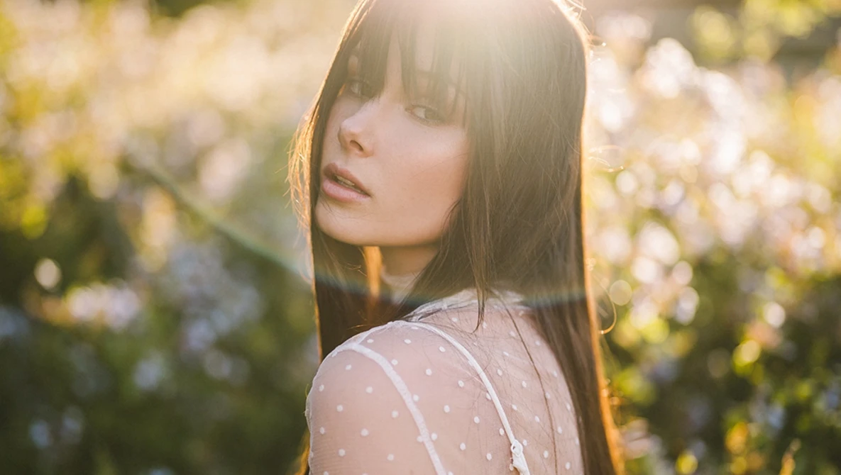 Woman with long dark hair in a garden of white flowers, backlit by golden sunlight.