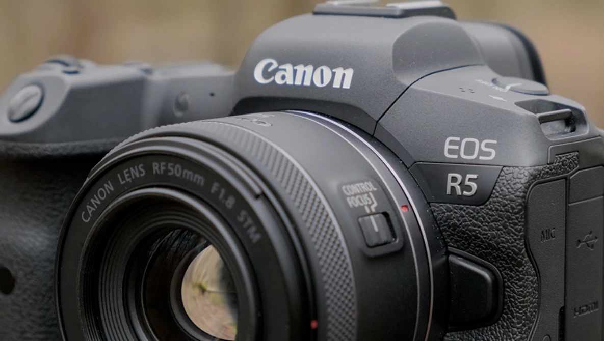 Canon EOS R5 mirrorless camera with Canon RF 50mm f/1.8 lens attached, shown in sharp focus against a blurred background.