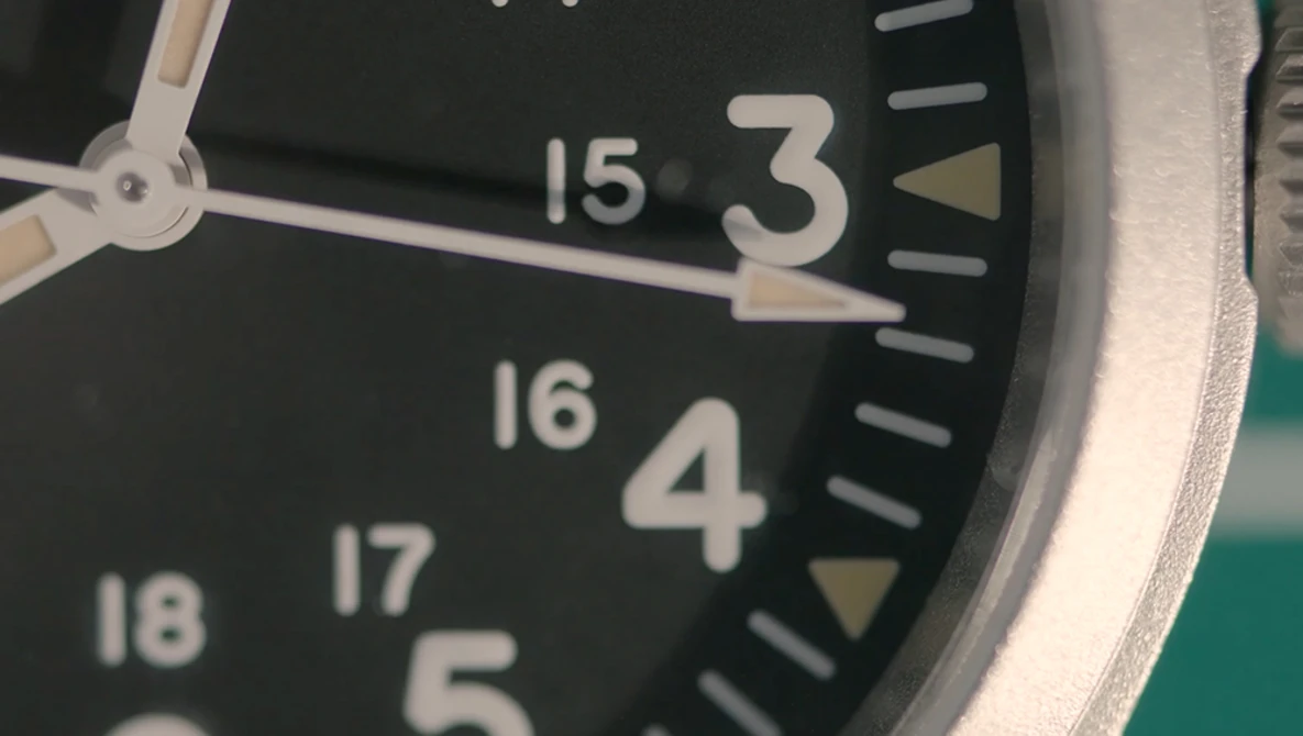 Close-up of a watch face with black dial, luminous hands, and numbered hour markers from 3 to 18.
