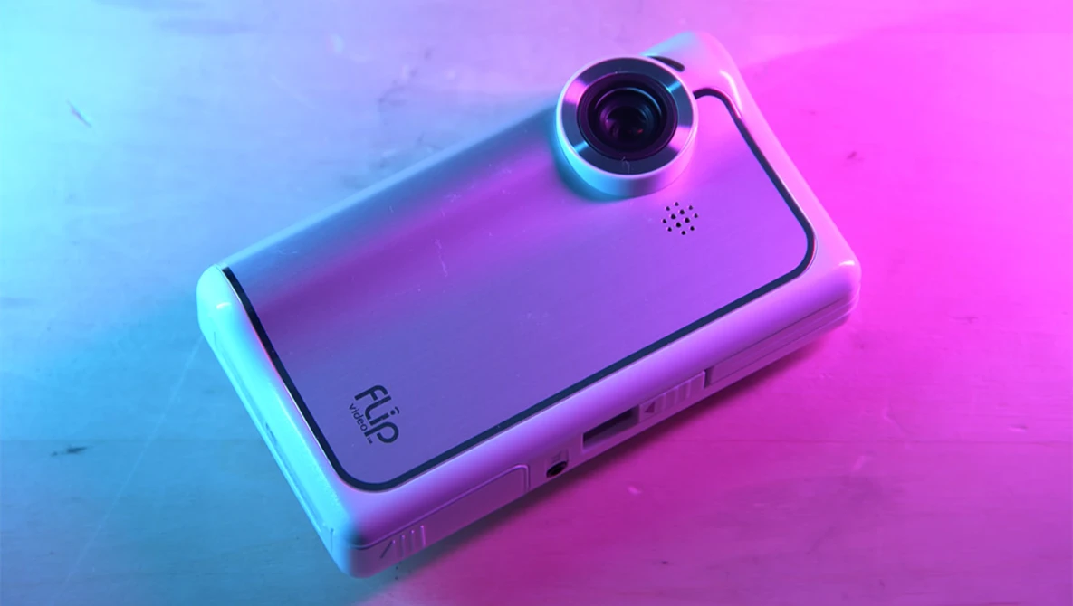 Compact camera device with prominent lens on vibrant neon blue and pink gradient background.