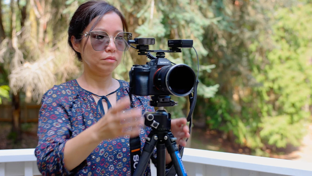 Cinematographer operating a cinema camera mounted on a tripod with follow focus gear in an outdoor garden setting.