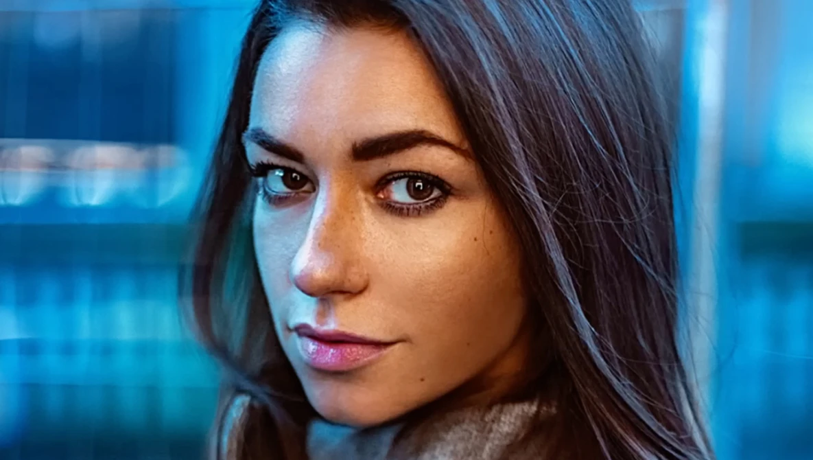 Woman with dark hair looking directly at camera against blue-tinted background.