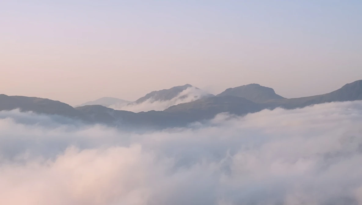 Mountain peaks rising above a sea of clouds at dawn, with soft purple and pink light illuminating the misty landscape.