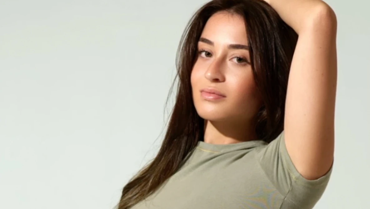 Woman with long dark hair in casual pose against neutral background.