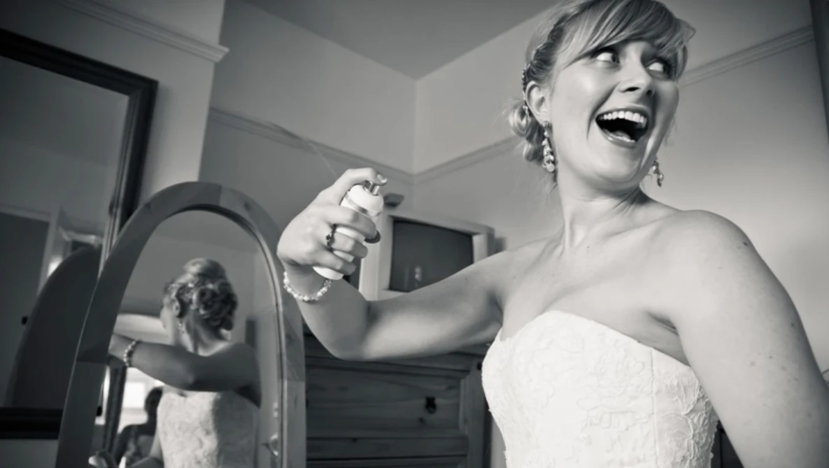 Bride in strapless wedding dress smiling while holding handheld mirror in black and white portrait.