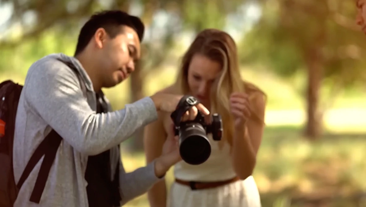 Male photographer showing a female subject a photo on the back of his DSLR camera outdoors.