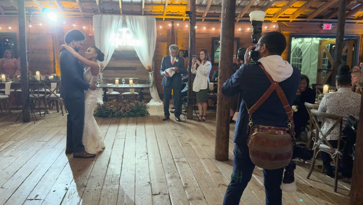 Bride and groom first dance at indoor wedding reception with guests watching from wooden floor venue.