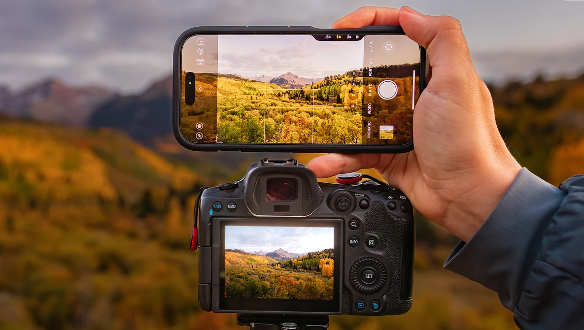 Smartphone and mirrorless camera displaying identical landscape photos of golden hillsides with mountains.