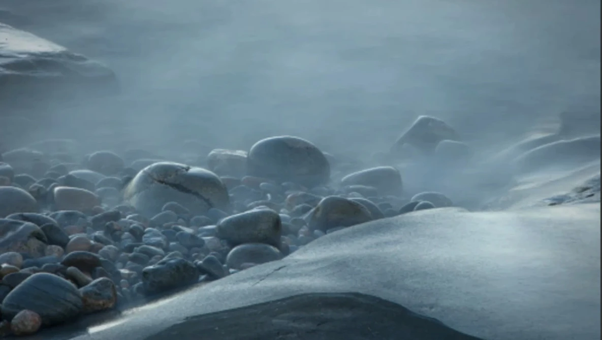 Snow-covered boulders shrouded in mist along a frozen coastline.