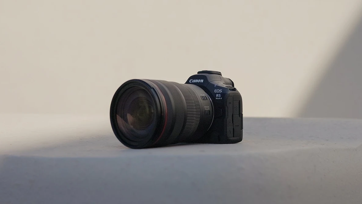 Canon EOS R5 mirrorless camera with attached telephoto lens on neutral surface.