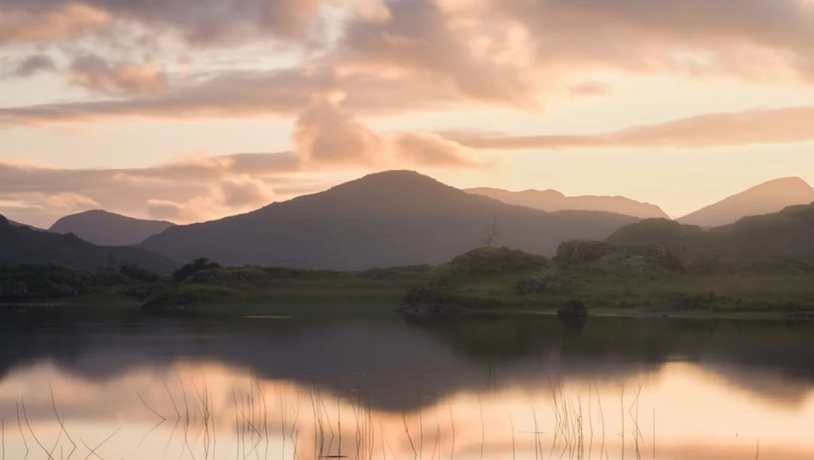 Mountain landscape reflected in still water at golden hour with warm, diffused light.
