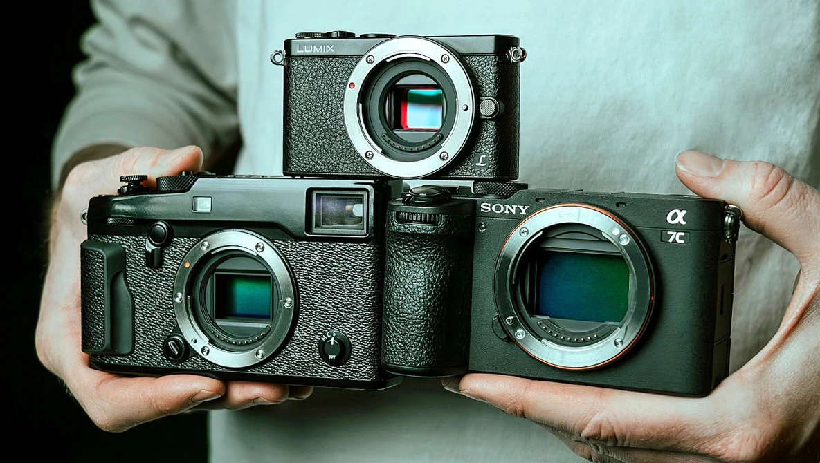 Three mirrorless cameras held in hands, showing sensor sizes from smallest to largest.