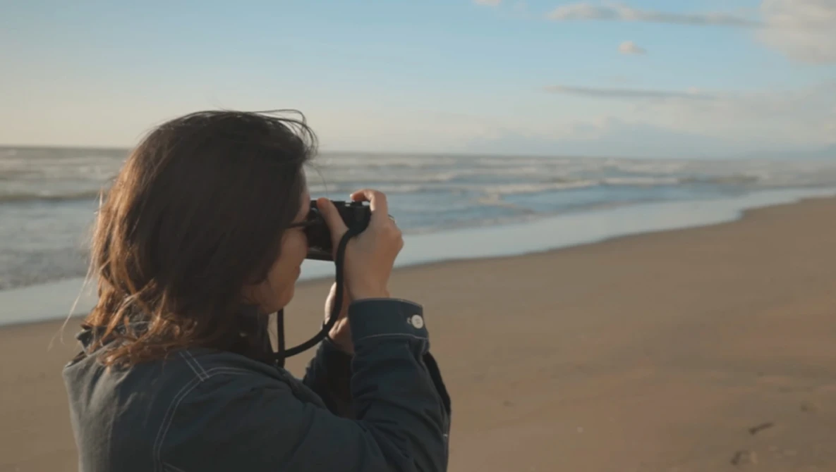 Woman photographing the ocean from a beach during golden hour.