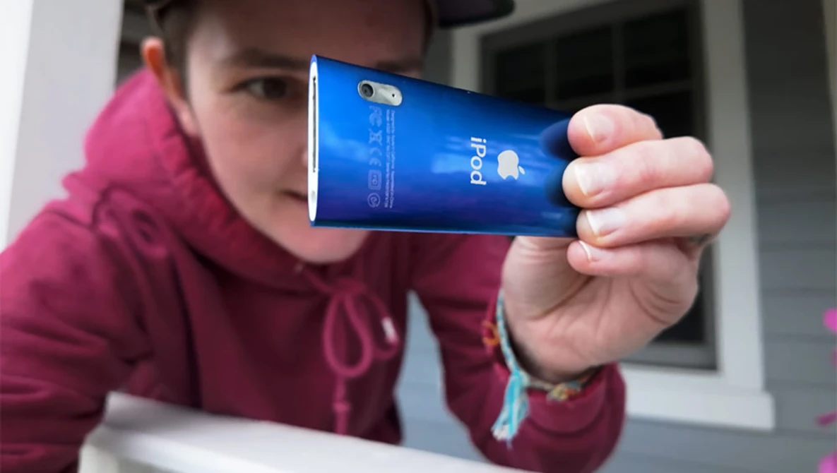 Person in burgundy hoodie holding blue smartphone displaying its rear case and camera.