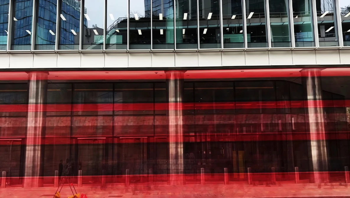 Modern building facade with vibrant red-tinted glass panels reflecting surrounding architecture and sky.