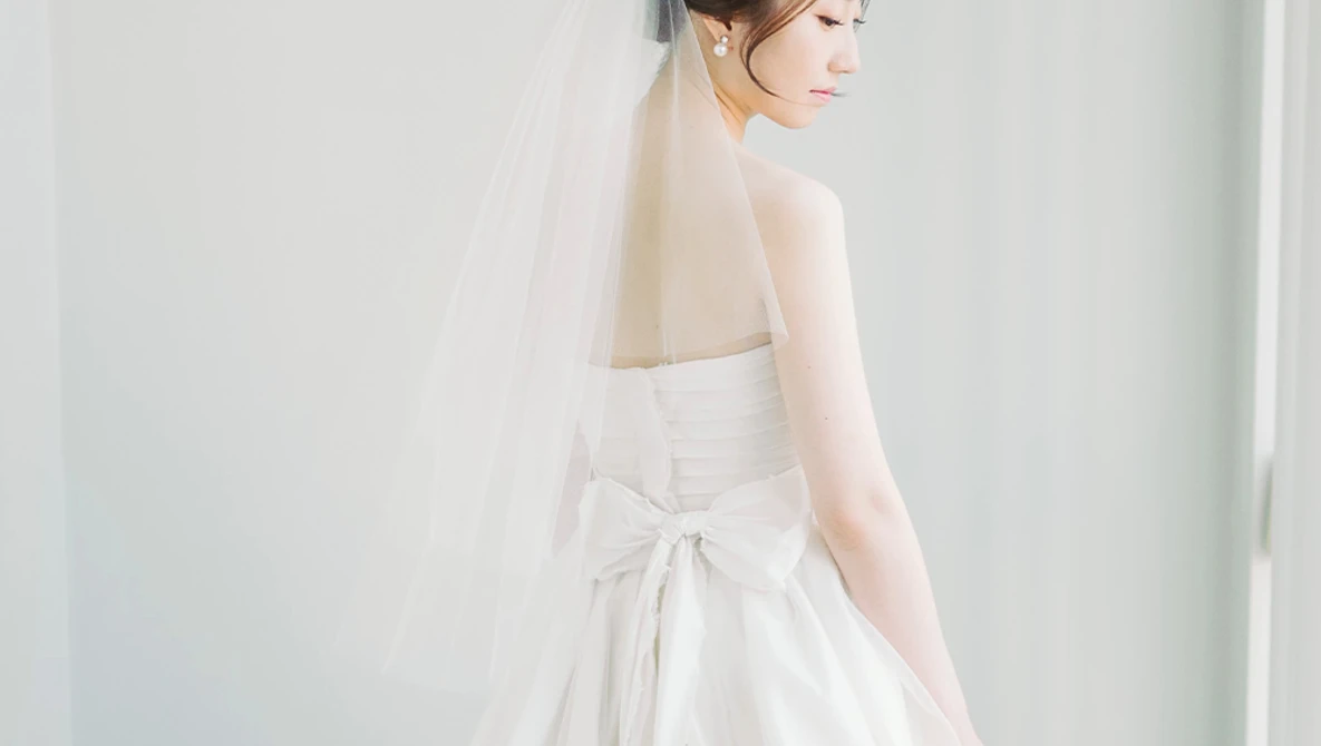 Bride in profile wearing a strapless white wedding dress with a bow detail and delicate veil.