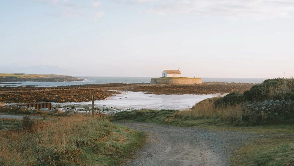 Isolated stone building with orange roof on distant headland overlooking tidal marshland and mudflats.