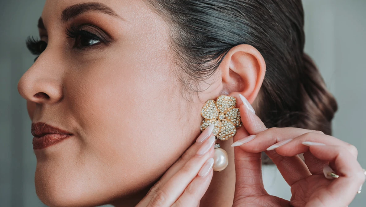 Woman in profile adjusting a pearl and crystal cluster earring near her ear.