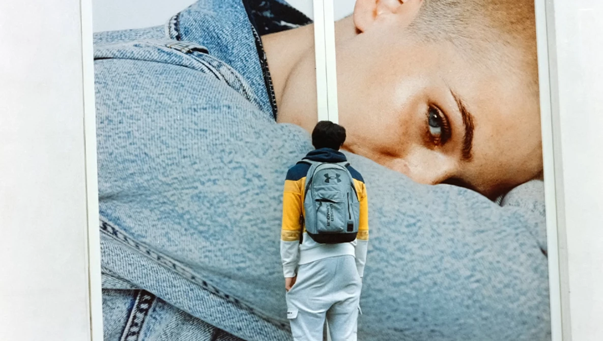 Person wearing backpack standing before large-scale portrait photography installation.