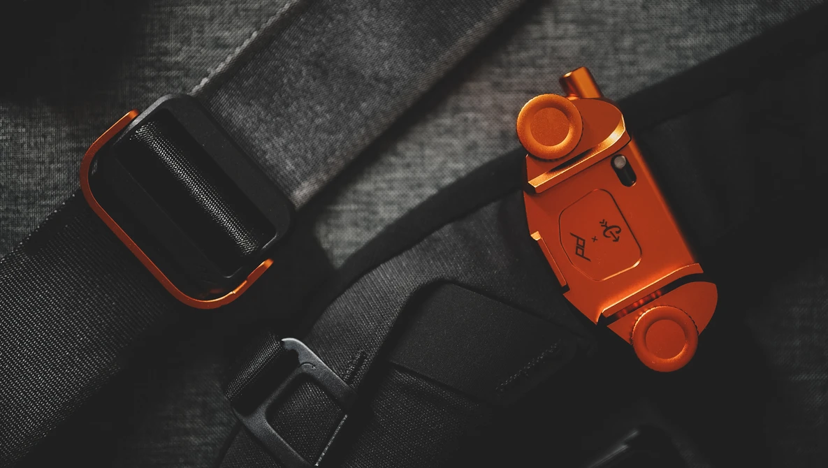 Orange and black camera equipment arranged on gray fabric with dramatic side lighting.