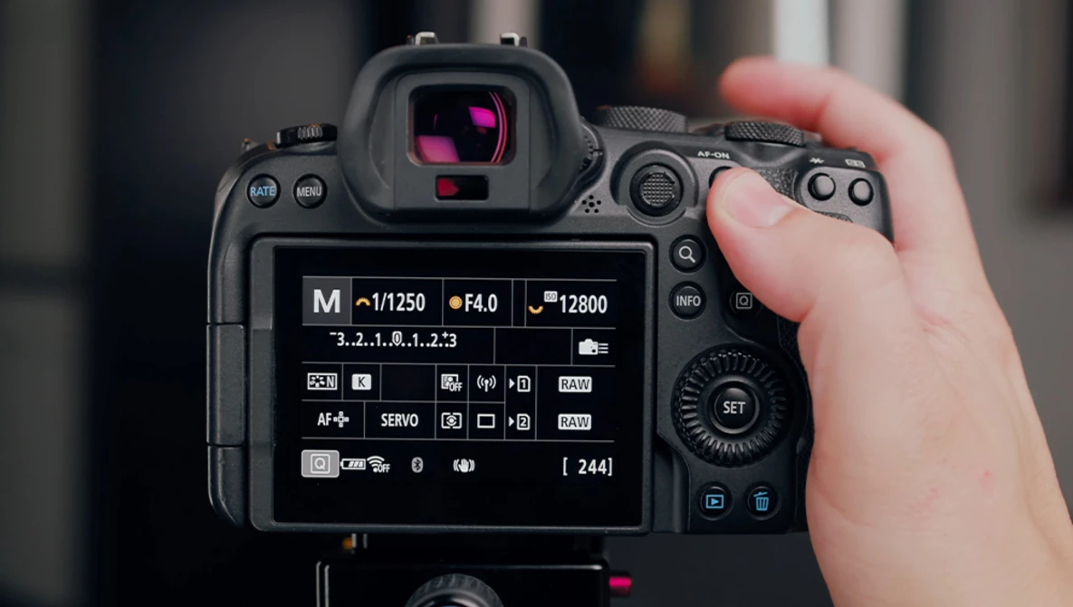 Photographer's hand holding a DSLR camera displaying exposure settings on the rear LCD screen.