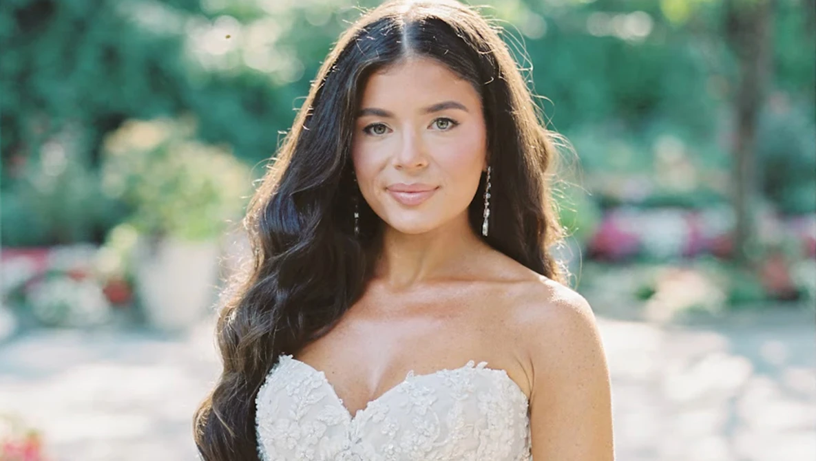 Woman in beaded white strapless gown with long dark wavy hair, photographed outdoors in natural sunlight.