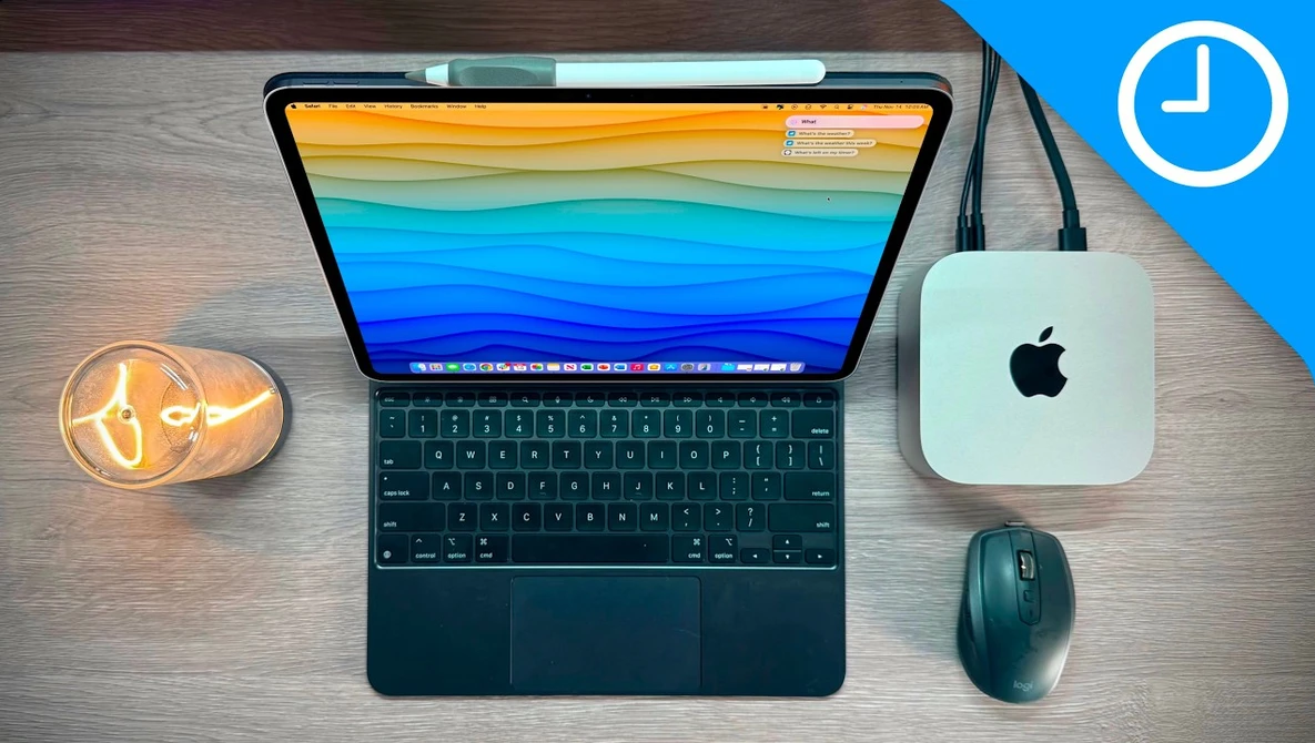 Flat lay of a tablet with colorful wallpaper, wireless mouse, Mac mini, and desk lamp on wood surface.