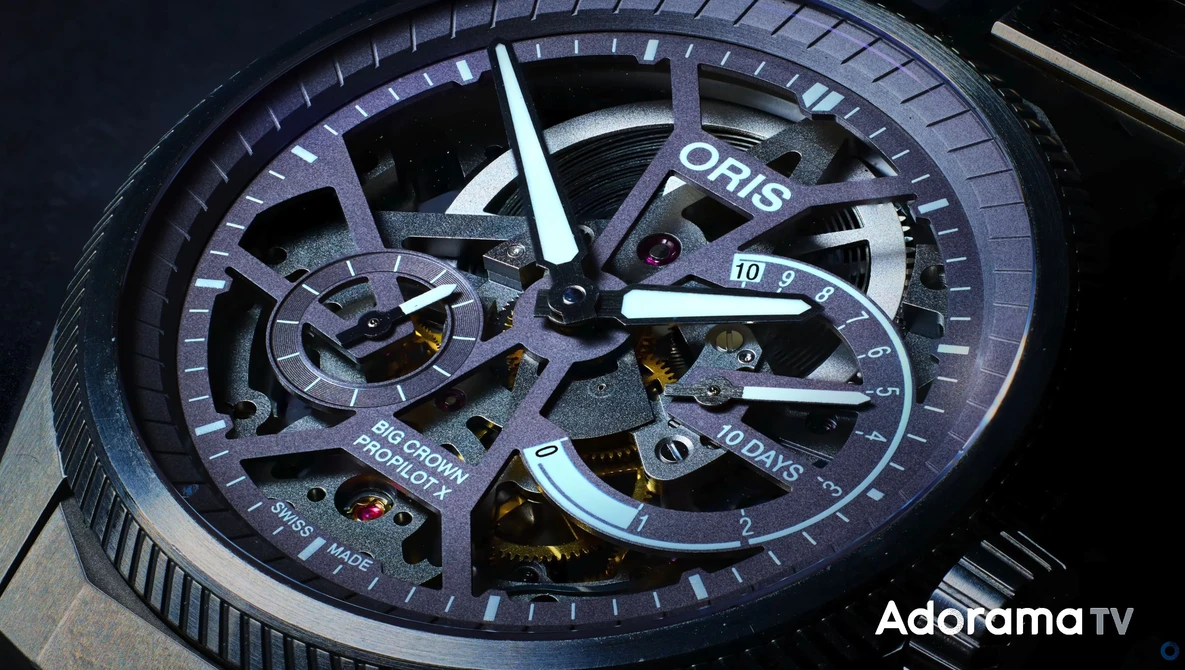 Close-up of an Oris luxury watch with exposed skeleton dial showing internal mechanisms and blue-toned case against dark background.