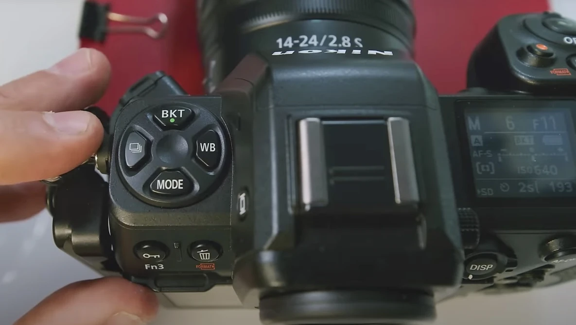 Close-up of camera control dial showing BKT, WB, and MODE buttons with lens labeled 14-24/2.8 S in background.